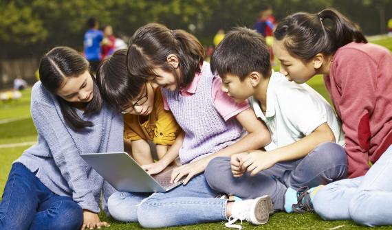 A group of children on a field looking at a laptop